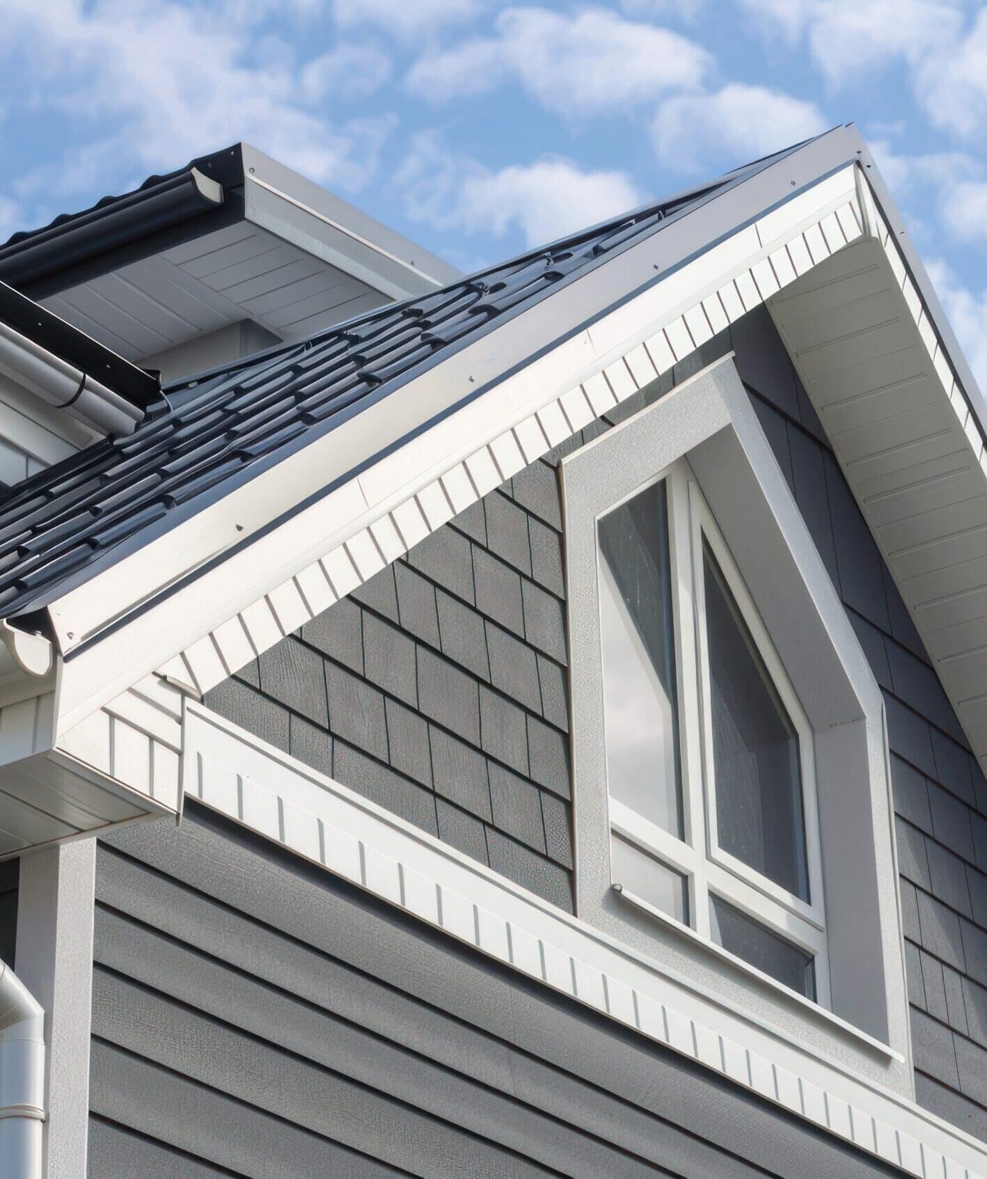 Gray zinc gutter on the facade of the house, white PVC downpipes and soffit paneling